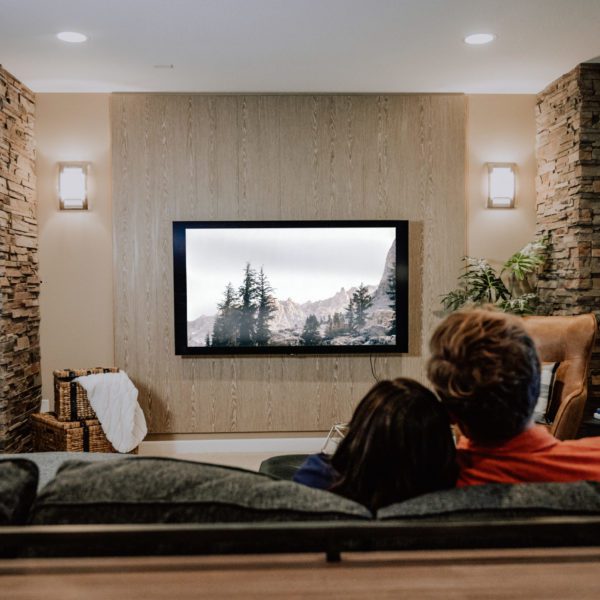 A couple enjoying a movie in their media room with an acoustic wood wall, stone fireplace, television, and a leather chair.